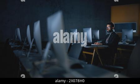 Concentrated Male Student Sitting Alone in College Informatics Room, Working Late Evenings on Computer Science Project. Young Scholar Study IT on Computer in University, Writing Code in Class. Stock Photo
