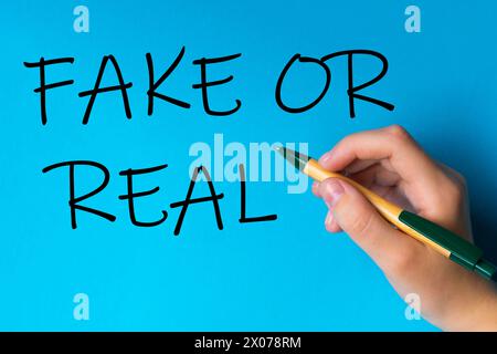 Children hand with pen write on an blue white background. Writing hand. Word Fake or real Stock Photo