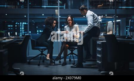 Diverse Team of Managers Working and Having Discussions in Big City Office in the Evening. Colleagues Talk, Discuss Business Opportunities, Evaluate Financial Reports, Plan Investment Strategy. Stock Photo
