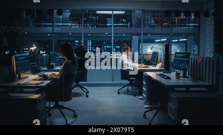 Diverse Team of Managers Working on Computers Behind Desks in Big City Office in the Evening. Colleagues Work, Creating Financial Reports, Play on Stock Market, Plan Investment Strategy. Stock Photo