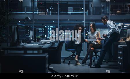 Diverse Team of Managers Working and Having Discussions in Big City Office in the Evening. Colleagues Talk, Discuss Business Opportunities, Evaluate Financial Reports, Plan Investment Strategy. Stock Photo