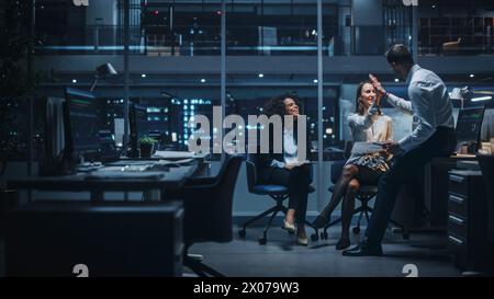 Diverse Team of Managers Working and Having Discussions in Big City Office in the Evening. Colleagues Talk, Discuss, Brainstorm Corporate Strategy, Giving High Five for Successful Idea. Stock Photo