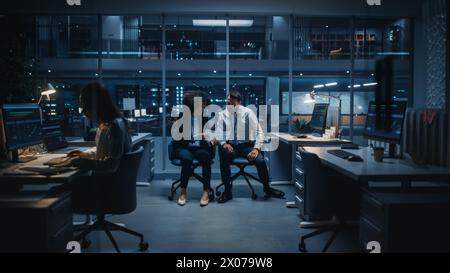 Diverse Team of Managers Working on Computers Behind Desks in Big City Office in the Evening. Colleagues Talk, Discuss Business Opportunities, Evaluate Financial Reports, Plan Investment Strategy. Stock Photo