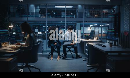 Diverse Team of Managers Working and Having Discussions in Big City Office in the Evening. Colleagues Talk, Discuss, Brainstorm Corporate Strategy, Giving High Five for Successful Idea. Stock Photo