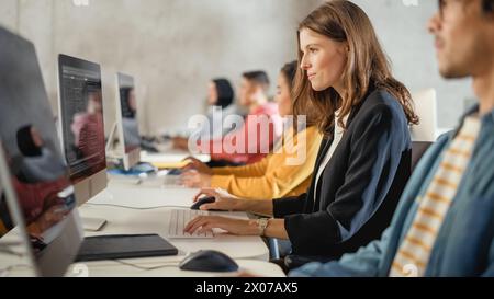Diverse Multiethnic Group of Female and Male Students Sitting in College Room, Learning Computer Science. Young Scholars Study Information Technology on Computers in University, Writing Code in Class. Stock Photo