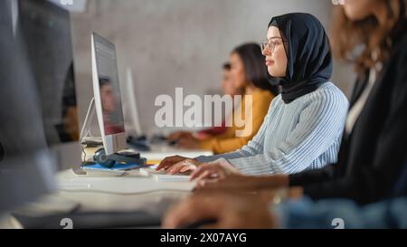 Happy Female Muslim Student Wearing a Hijab, Studying in Modern University with Diverse Multiethnic Classmates. Students Successfully Learn Computer Science, Writing Software Code. Stock Photo
