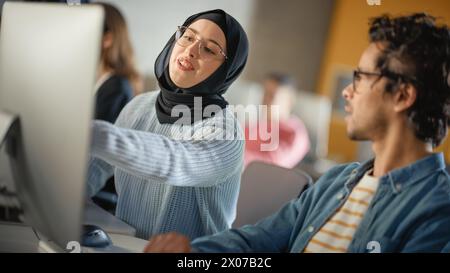 Female Muslim Student Wearing Hijab, Studying in Modern University with Diverse Multiethnic Classmates. She Asks Scholar a Question in College Room. Learning Software Engineering or Computer Science. Stock Photo