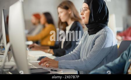 Curious Female Muslim Student Wearing a Hijab, Studying in Modern University with Diverse Multiethnic Classmates. College Scholars Work in College Room, Learning IT, Programming or Computer Science. Stock Photo