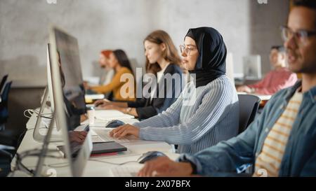 Diverse Multiethnic Group of Female and Male Students Sitting in College Room, Learning Computer Science. Young Scholars Study Information Technology on Computers in University, Writing Code in Class. Stock Photo