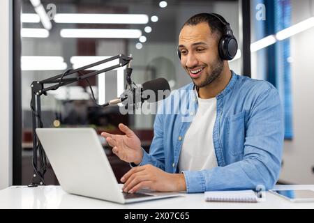 Focused Indian man records a podcast from his stylish living room, representing modern home-working scenarios. Stock Photo