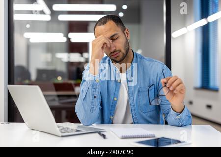Indian man in living room setting appearing stressed with work, showing signs of a worker overwhelmed by business matters. Stock Photo