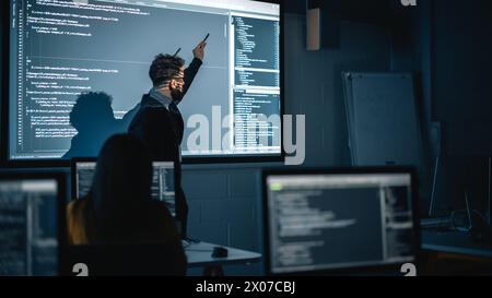 Teacher Giving Computer Science Lecture to Diverse Multiethnic Group of Female and Male Students in Dark College Room. Projecting Slideshow with Programming Code. Explaining Information Technology. Stock Photo