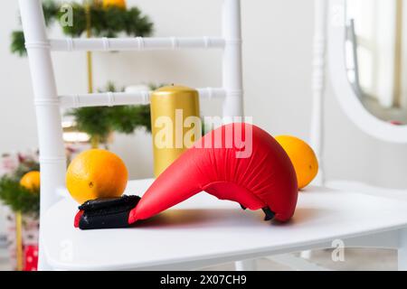 Sports equipment: dumbbell, boxing gloves, fir branch, Christmas ornament, gifts on chair. Stock Photo