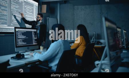 Teacher Giving Computer Science Lecture to Diverse Multiethnic Group of Female and Male Students in Dark College Room. Projecting Slideshow with Programming Code. Explaining Information Technology. Stock Photo