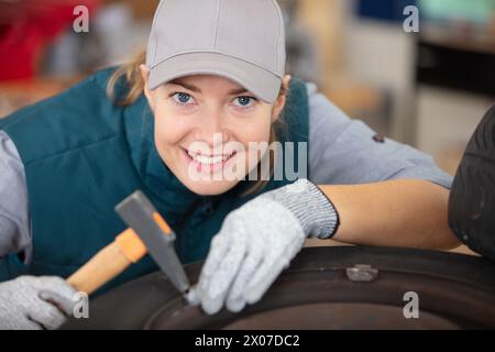 female mechanic using a hammer while working on a tyre Stock Photo