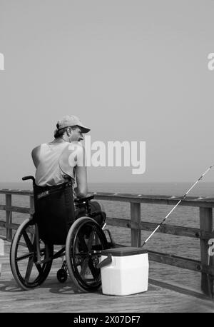 Man in wheelchair fishes at Chesapeake Bay Virginia USA Stock Photo