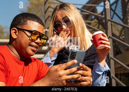Happy interracial couple checking cell phone outdoors. Stock Photo