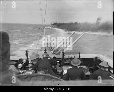 ROYAL NAVY CONVOY FROM ALEXANDRIA TO MALTA MEETS AND ENGAGES ITALIAN WARSHIPS IN THE MEDITERRANEAN, 22 MARCH 1942 - HMS CLEOPATRA throws out smoke to shield the convoy as HMS EURYALUS elevates her forward 5.25 inch guns to shell the Italian Fleet  Royal Navy, CLEOPATRA (HMS), Royal Navy, HMS Euryalus, Light Cruiser, (1939) Stock Photo