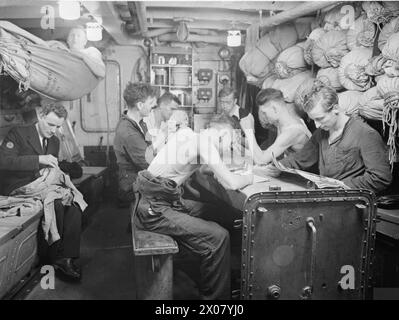 LIFE ON BOARD HM CORVETTE WIDGEON, AUGUST 1943, IN THE NORTH SEA AND AT HARWICH, MEN OF THE CORVETTE WIDGEON GO ABOUT THE EVERYDAY JOBS OF THEIR WARTIME ROUTINE. - Mess-deck scene at sea. While the card party proceeds, one man rests in his hammock, another repairs his clothes (left) and others write letters home or read  Royal Navy, HMS Wigtown Bay, Frigate, (1945) Stock Photo