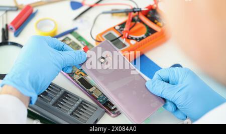 Technician repairs broken smartphone at table in workshop Stock Photo