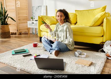 A teenage girl sitting on the floor, fully focused on her laptop, engaged in e-learning at home. Stock Photo