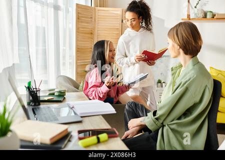 A diverse group of teenage girls of different ethnicities and backgrounds are gathered around a table, studying together from home. Stock Photo