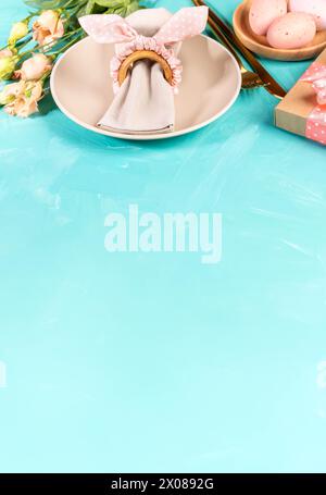 Easter pastel peach color table serving menu template on turquoise. Plates, eggs, napkin, napkin ring with bunny ears, golden cutlery, Eustoma flowers Stock Photo
