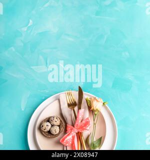 Serving of Easter table top view. Beige plates, nest with quail eggs of natural colors, golden cutlery, delicate Eustoma flower on turquoise. Holiday Stock Photo