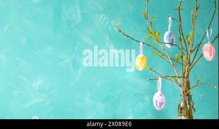 Holiday card template. Easter tree on turquoise background. Decorative pastel color eggs hanging on spring twigs with young leaves. Creative Easter im Stock Photo