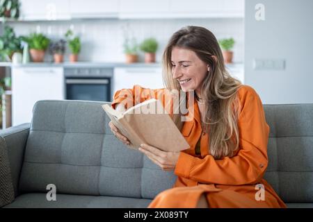 Interested woman reading novel book smiling enjoy calmness weekend tranquil time at home sit on sofa Stock Photo