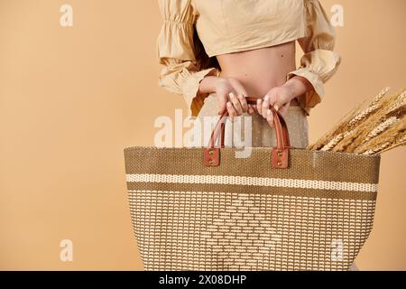 A young woman with long brunette hair elegantly holding a large, hand-crafted bag in a studio setting, exuding a summery vibe. Stock Photo