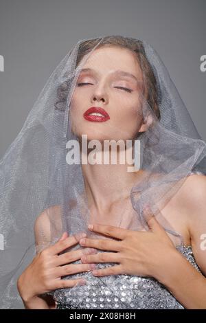 A young woman exudes classic beauty while posing in a studio, wearing a veil on her head. Stock Photo