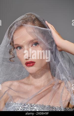 A young woman exudes classic beauty as she poses with a veil draped delicately over her head in a studio setting. Stock Photo