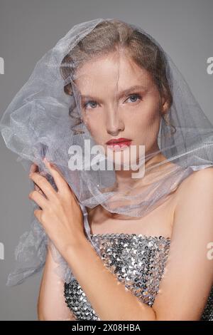 A young woman exudes classic beauty, posing in a studio with a graceful veil atop her head. Stock Photo