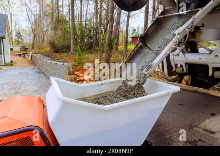 Construction site displays wet cement coming out of cement truck chute into concrete buggy driven by wheelbarrow Stock Photo