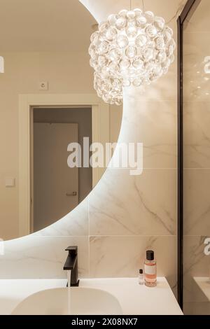 A stylish modern bathroom featuring a unique glass orb chandelier, marble walls, and a sleek sink with cosmetics Stock Photo