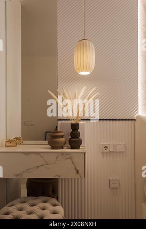A cozy corner with a chic pendant lamp, dried pampas grass, and sophisticated pottery on a marble table against a textured wall Stock Photo