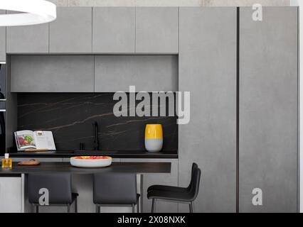 A contemporary kitchen featuring sleek grey cabinetry, black marble backsplash, and a vibrant yellow decorative jar Stock Photo