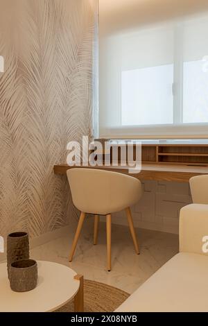 A cozy modern home office environment featuring a sleek wooden desk, comfortable beige chairs, patterned wallpaper, and natural light filtering throug Stock Photo