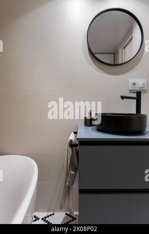 Modern bathroom interior with a round mirror, black washbasin, and decorative pebble floor accents Stock Photo