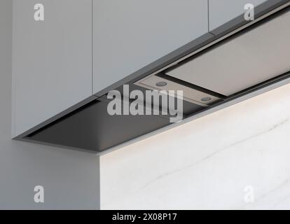 An elegant and contemporary kitchen extractor hood integrated into a cabinet, displayed in a minimalist home setting Stock Photo