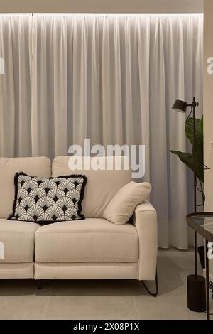 Elegant living room interior with a cozy beige sofa, decorative pillow, and stylish floor lamp by the curtains Stock Photo