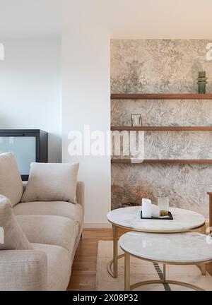 Cozy and modern living room corner featuring a plush sofa, marble coffee tables, and decorative shelving with floral wallpaper Stock Photo