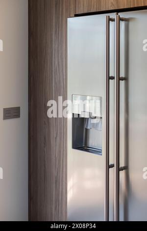 A stylish modern kitchen corner featuring a stainless steel double-door refrigerator with a built-in water and ice dispenser Stock Photo