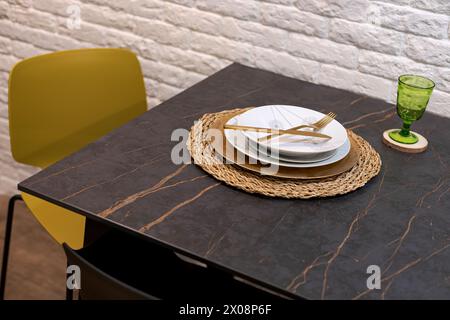 Elegant table setting with white plates, gold cutlery, and a green glass on a marble table Stock Photo