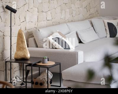 Modern living room interior with beige couch, patterned pillows, and stone wall backdrop Stock Photo