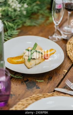 A delicately cooked fish fillet served with fresh asparagus and a smooth puree, plated on white china against a rustic wooden table backdrop Stock Photo
