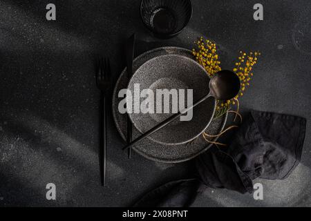 Top view of a sophisticated black table setting featuring dark plates, utensils, and a yellow mimosa garnish. Stock Photo