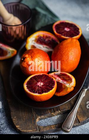 Vibrant blood oranges, some sliced, arranged on a dark rustic plate alongside vintage cutlery, evoking a fresh and natural feel Stock Photo