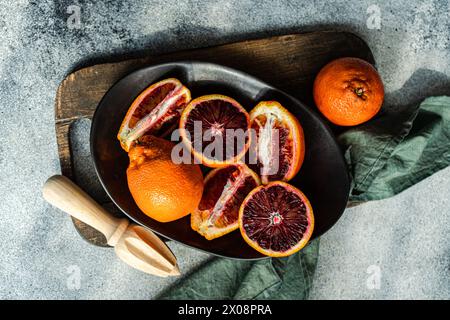 A top view of juicy blood oranges, freshly cut and displayed on a dark plate with a rustic wooden board background Stock Photo
